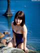 A woman in a blue bathing suit sitting on a log by the water.