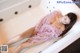 A woman in a pink dress laying in a bathtub.