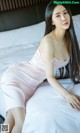 A woman in a pink dress sitting on a bed.