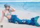 A woman in a mermaid costume laying on the beach.